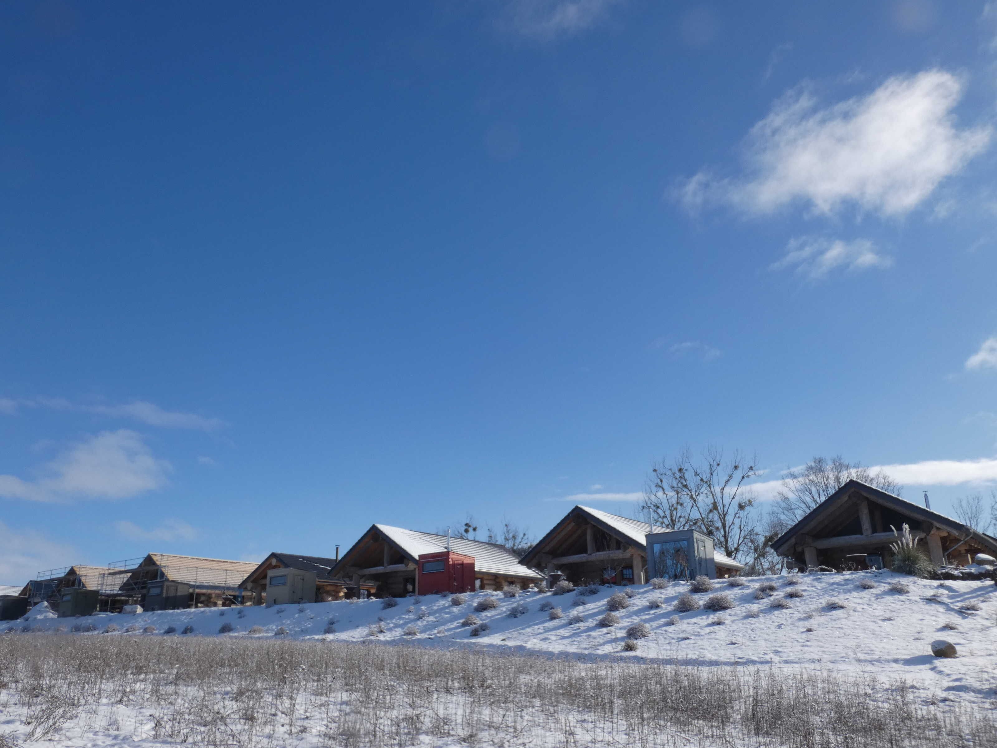 Eine Reihe von Hütten vor einer verschneiten Landschaft und blauem Himmel.