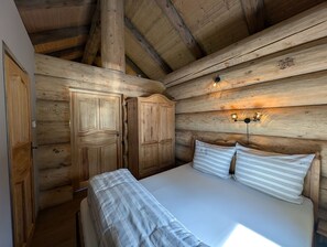 A wooden cabin room with a bed, two wardrobes, and a wall-mounted light fixture.