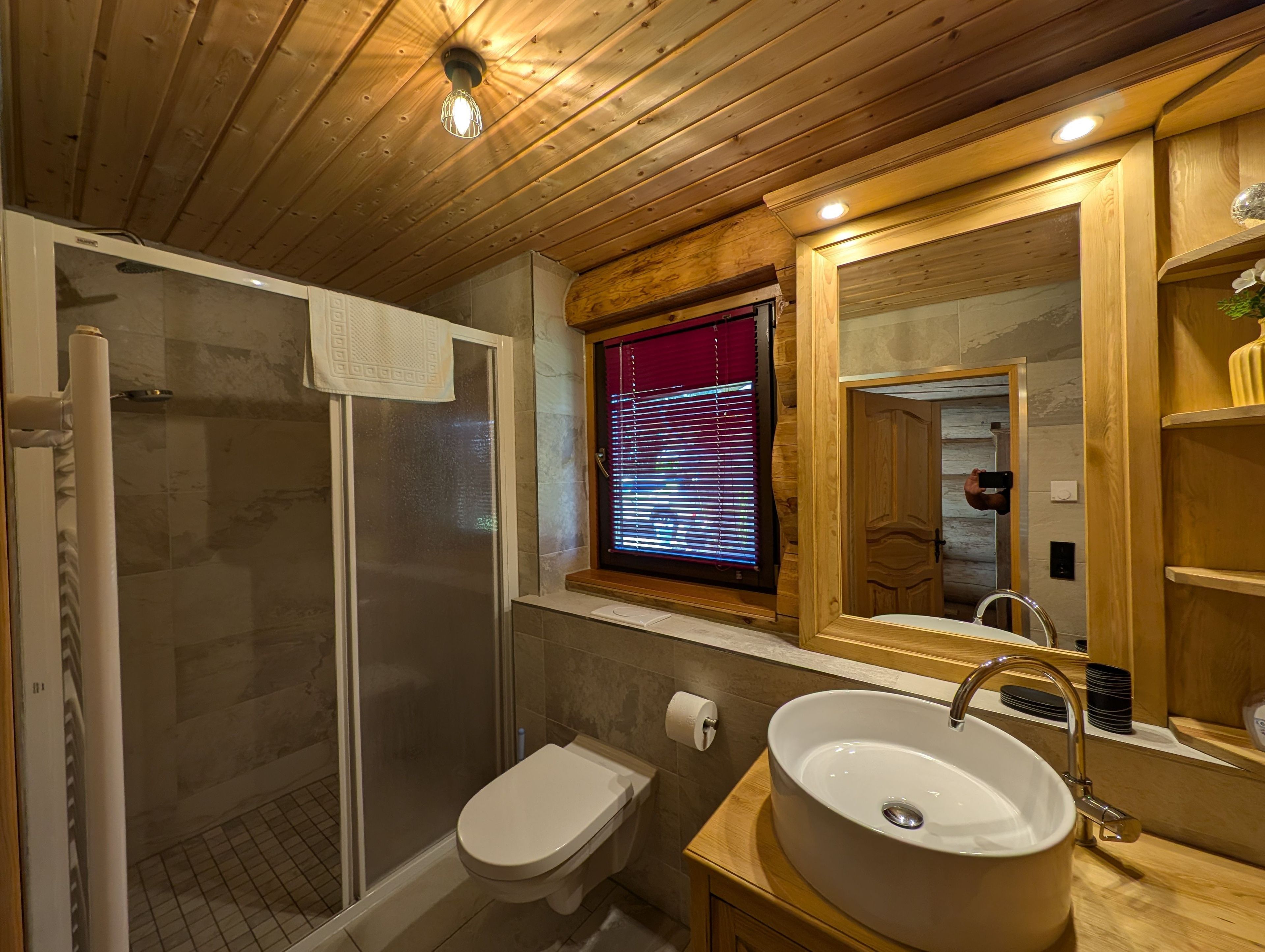 Un bagno con doccia vetrata, un water, un lavandino con specchio e una finestra con persiane.