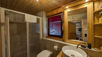 Un bagno con doccia vetrata, un water, un lavandino con specchio e una finestra con persiane.