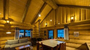 Ein rustikales Blockhaus-Interieur mit einer Couch, einem Esstisch, Stühlen und einem Kamin.