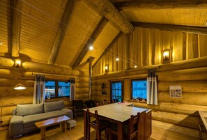 A log cabin interior with a sofa, dining table, chairs, and a fireplace.