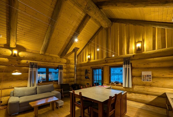 A log cabin interior with a sofa, dining table, chairs, and a fireplace.