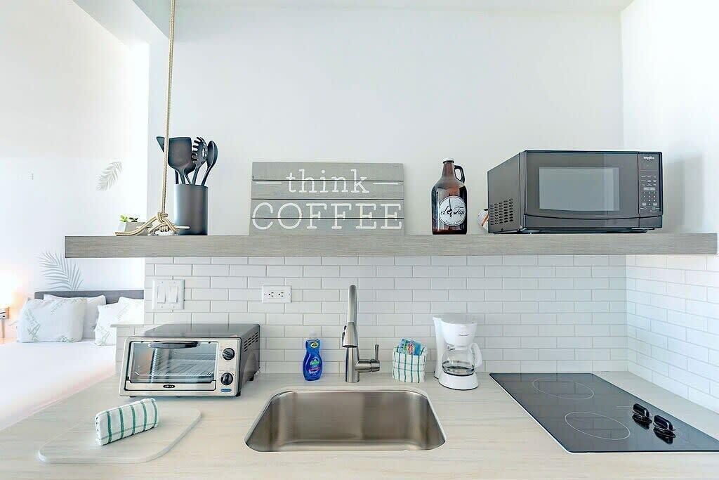 Una cocina moderna con un lavamanos de acero inoxidable, horno empotrado, microondas y cafetera. Hay un letrero en la pared que dice "think COFFEE".
