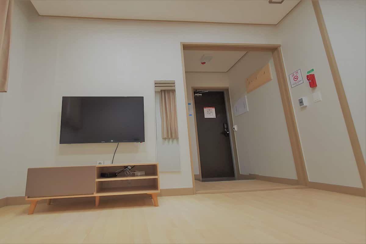 Une pièce avec un téléviseur fixé au mur, un meuble de rangement en bois, une porte équipée d’un détecteur d’incendie et un interrupteur.