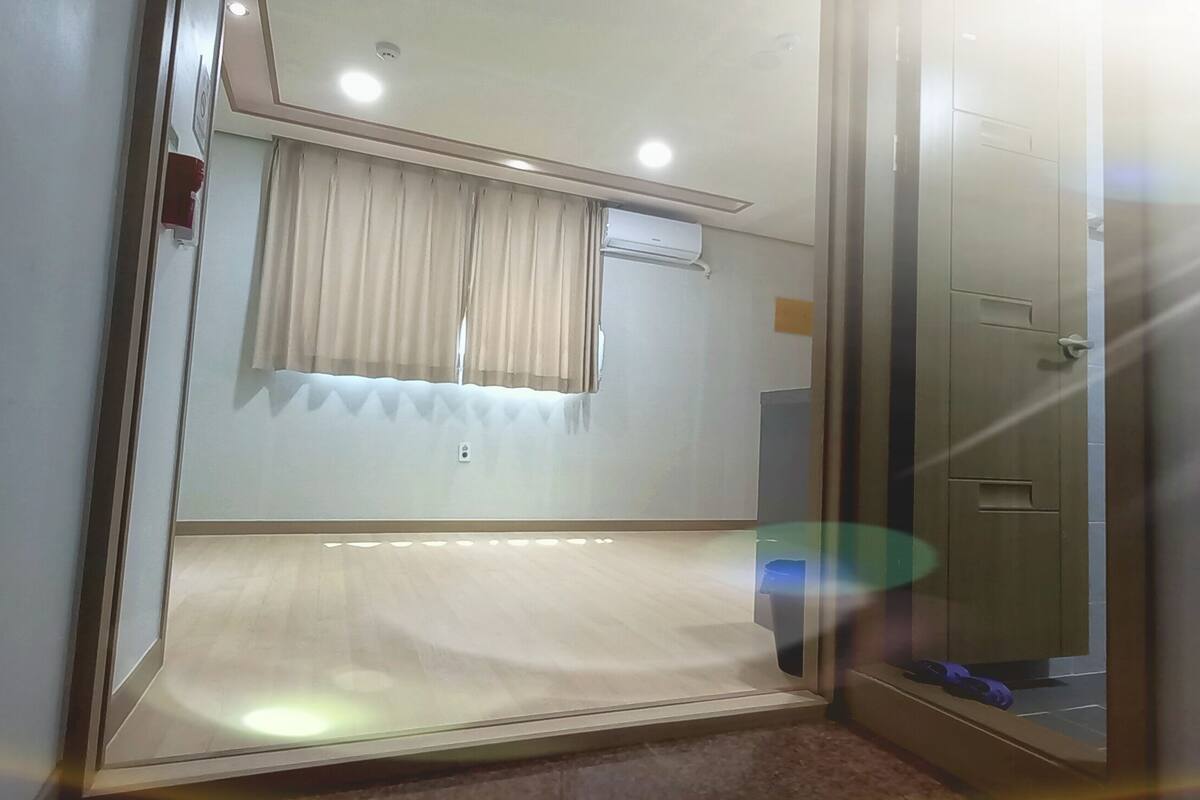 Une chambre d’hôtel avec un lit, une fenêtre avec des rideaux, un luminaire au plafond et une porte.