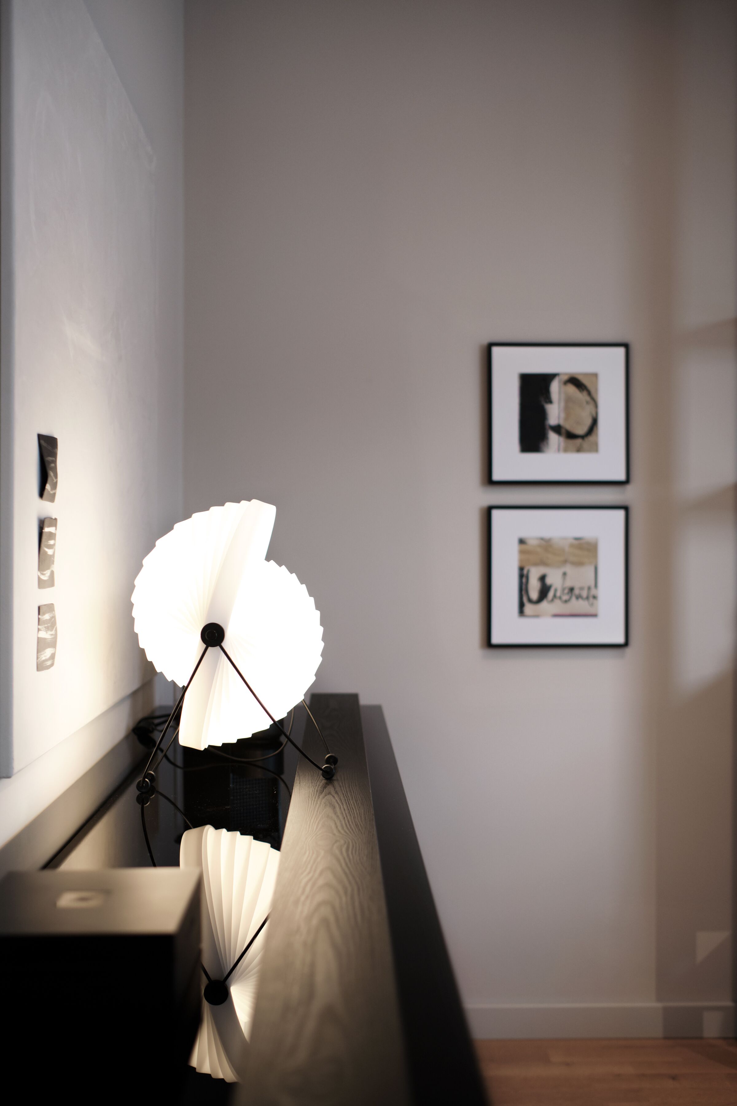 Ein modernes Zimmer mit Schreibtischlampe, gerahmtem Kunstwerk an der Wand und einem Fenster mit Jalousien.