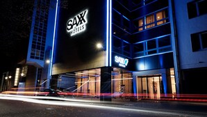 Un hôtel reconnaissable à son grand panneau « SAX Hotels », à ses larges fenêtres et à sa façade moderne.