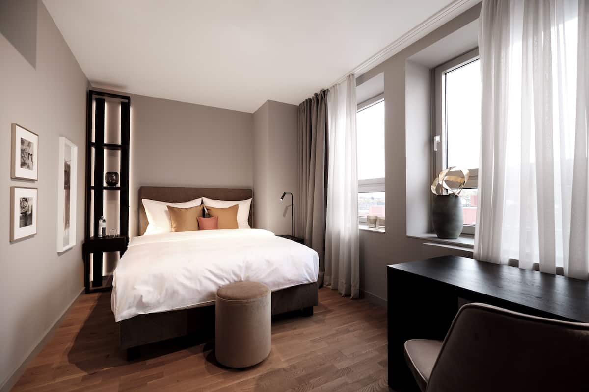 Une chambre d’hôtel moderne, dotée d’un grand lit, d’un bureau et d’une fenêtre avec des rideaux.