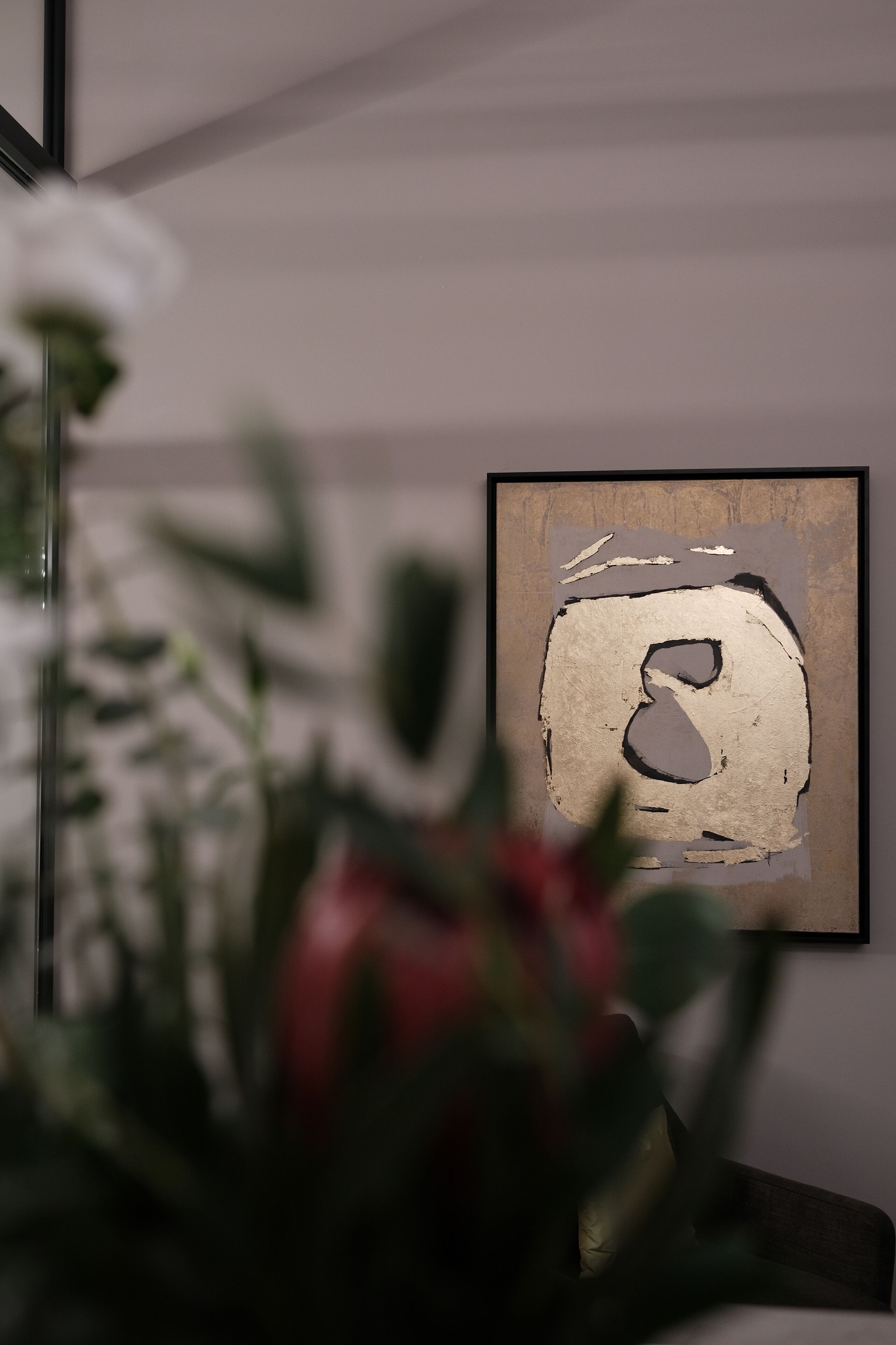 A framed artwork on a wall with a blurred foreground of a plant.