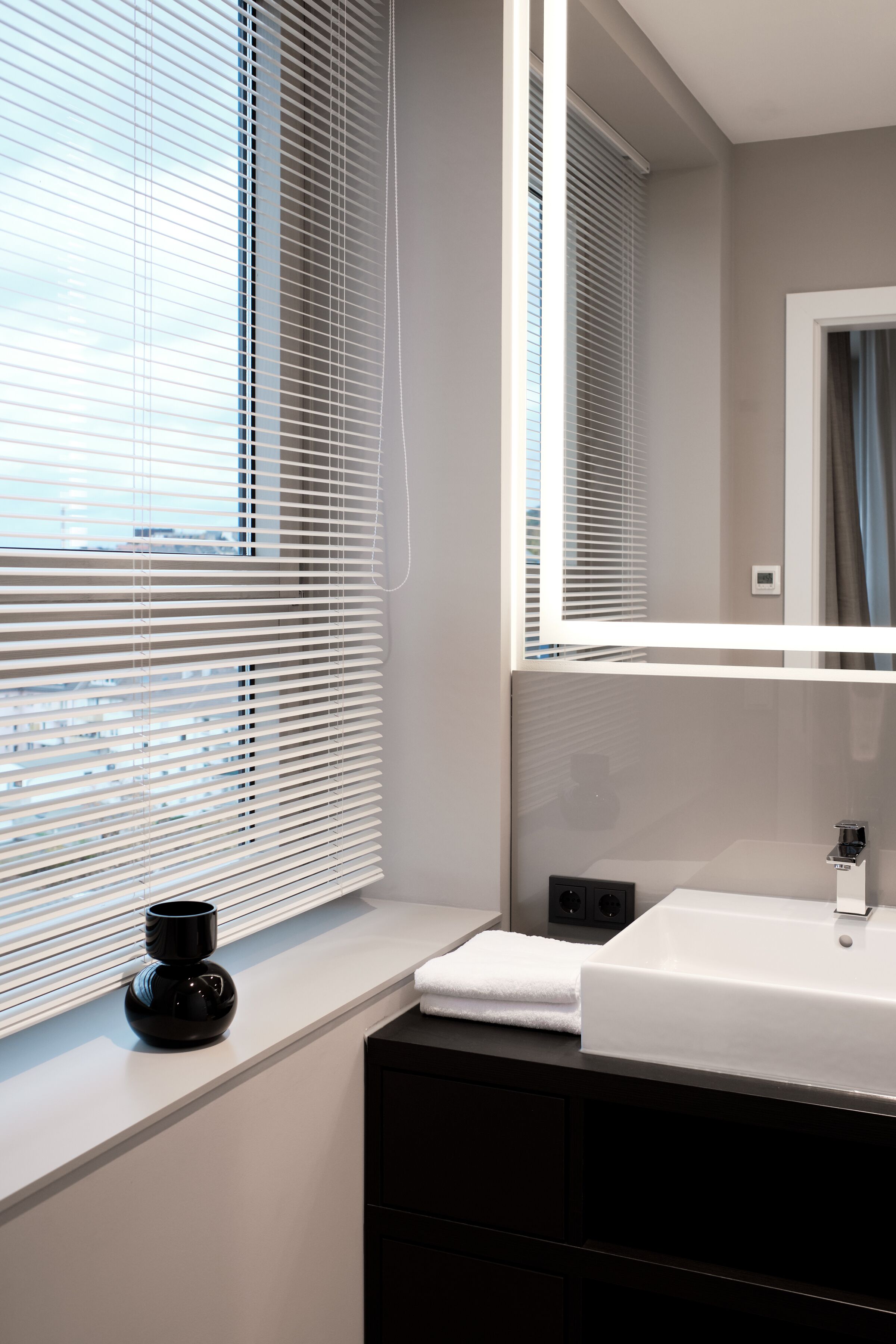Ein modernes Badezimmer mit großem Fenster, einem weißen Waschbecken und einem schwarzen Schrank.