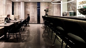 Un restaurant moderne doté d’un bar, de murs en marbre et d’un espace détente comprenant un canapé et des tables.