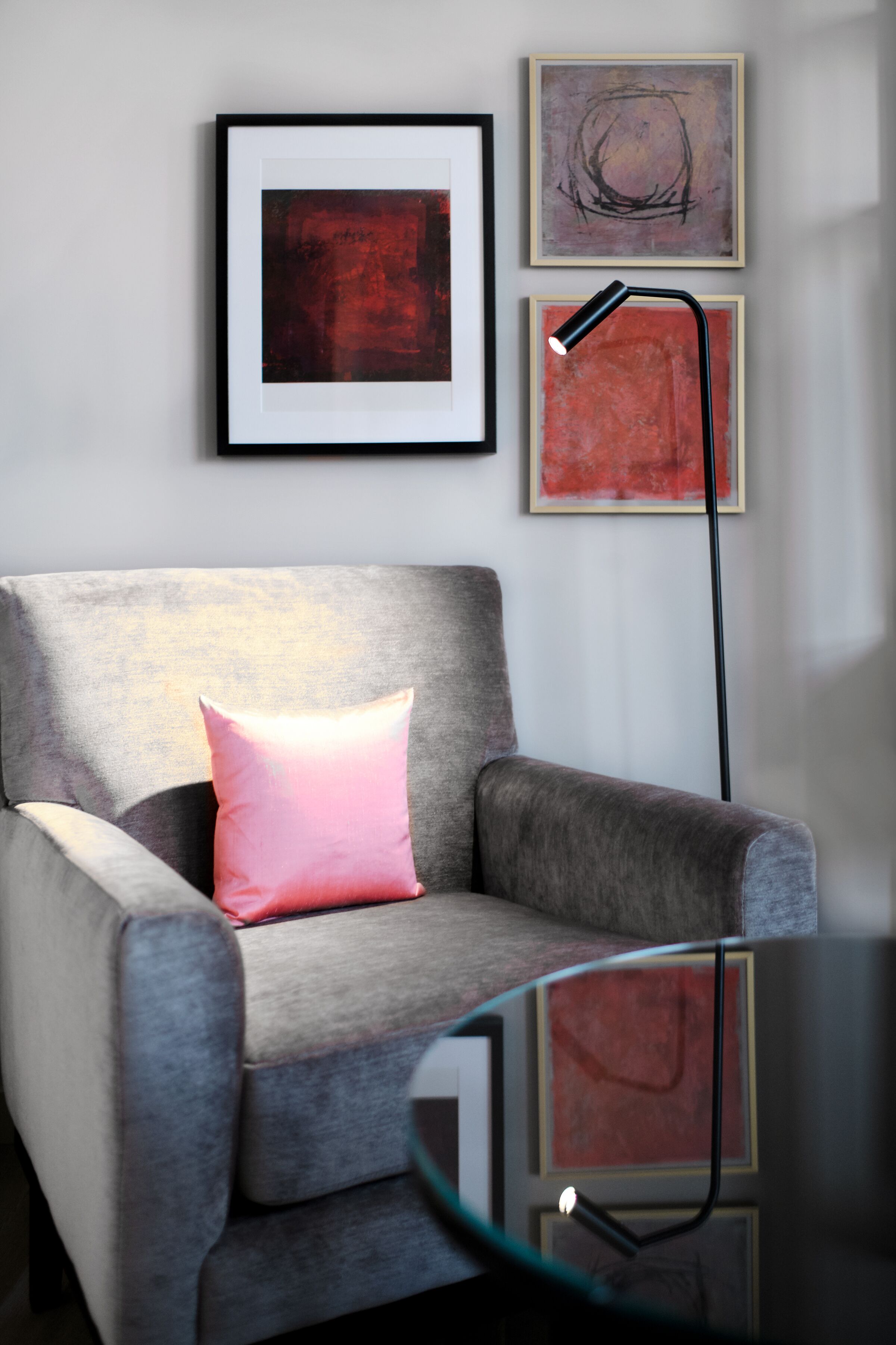 Een moderne woonkamer met een grijze fauteuil, een roze kussen en abstracte kunst aan de muur.