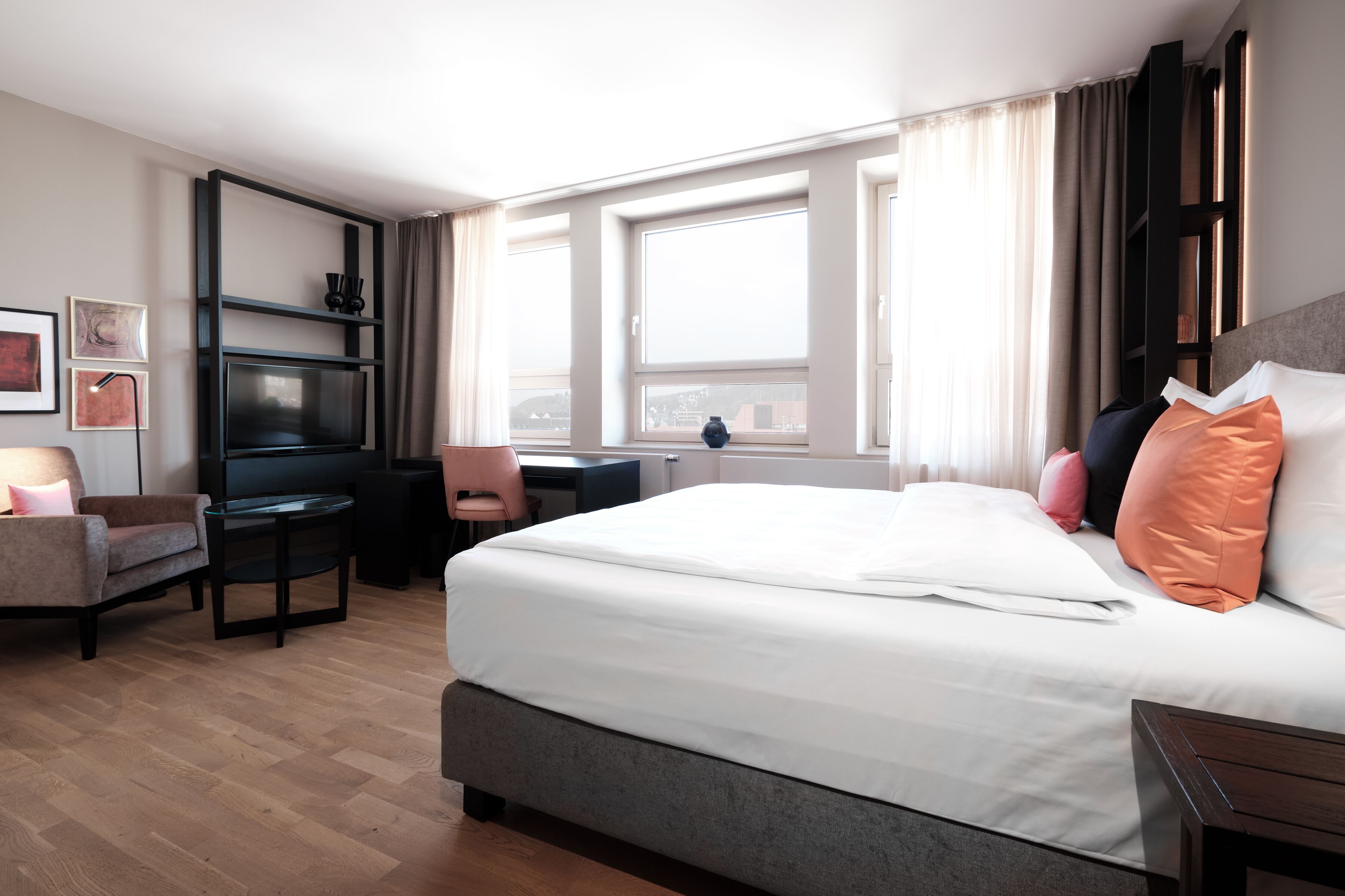 A modern hotel room with a large bed, a desk, a chair, and a TV.