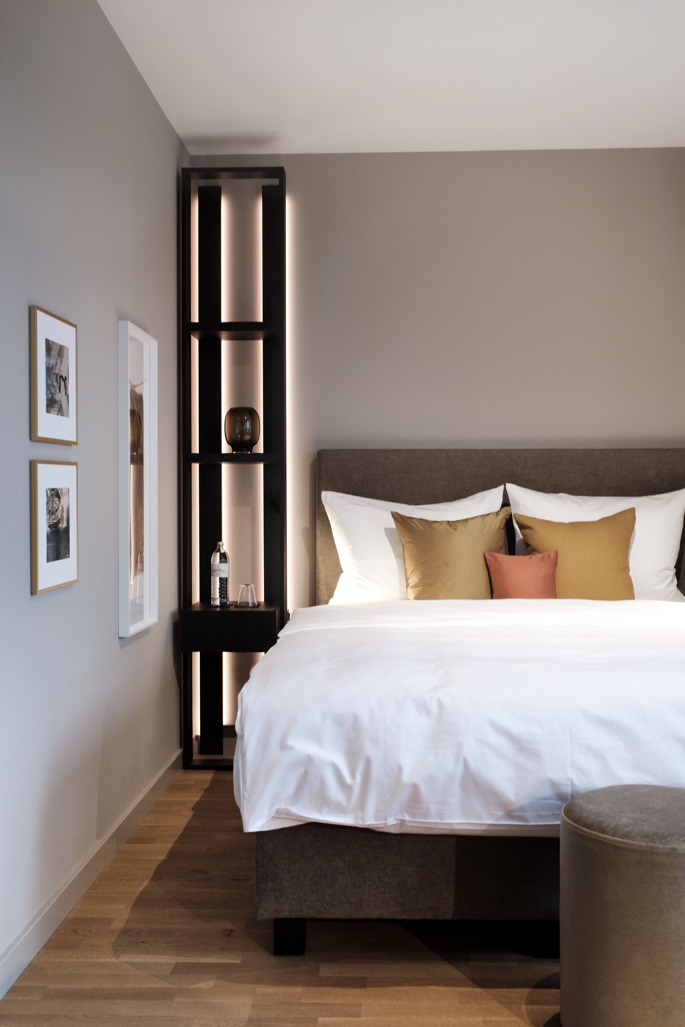 Una habitación de hotel moderna con una cama grande, una mesita de noche y un mueble de estanterías integrado.