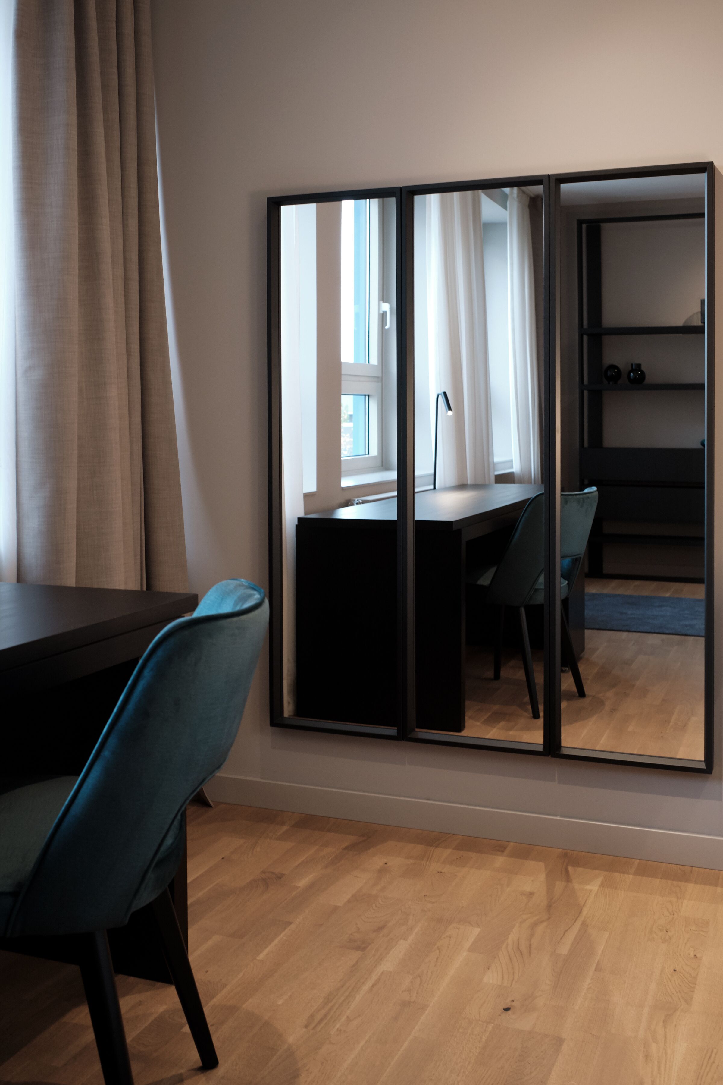 Une pièce avec un plancher en bois, une table à manger avec des chaises, un grand miroir et une fenêtre avec des rideaux.