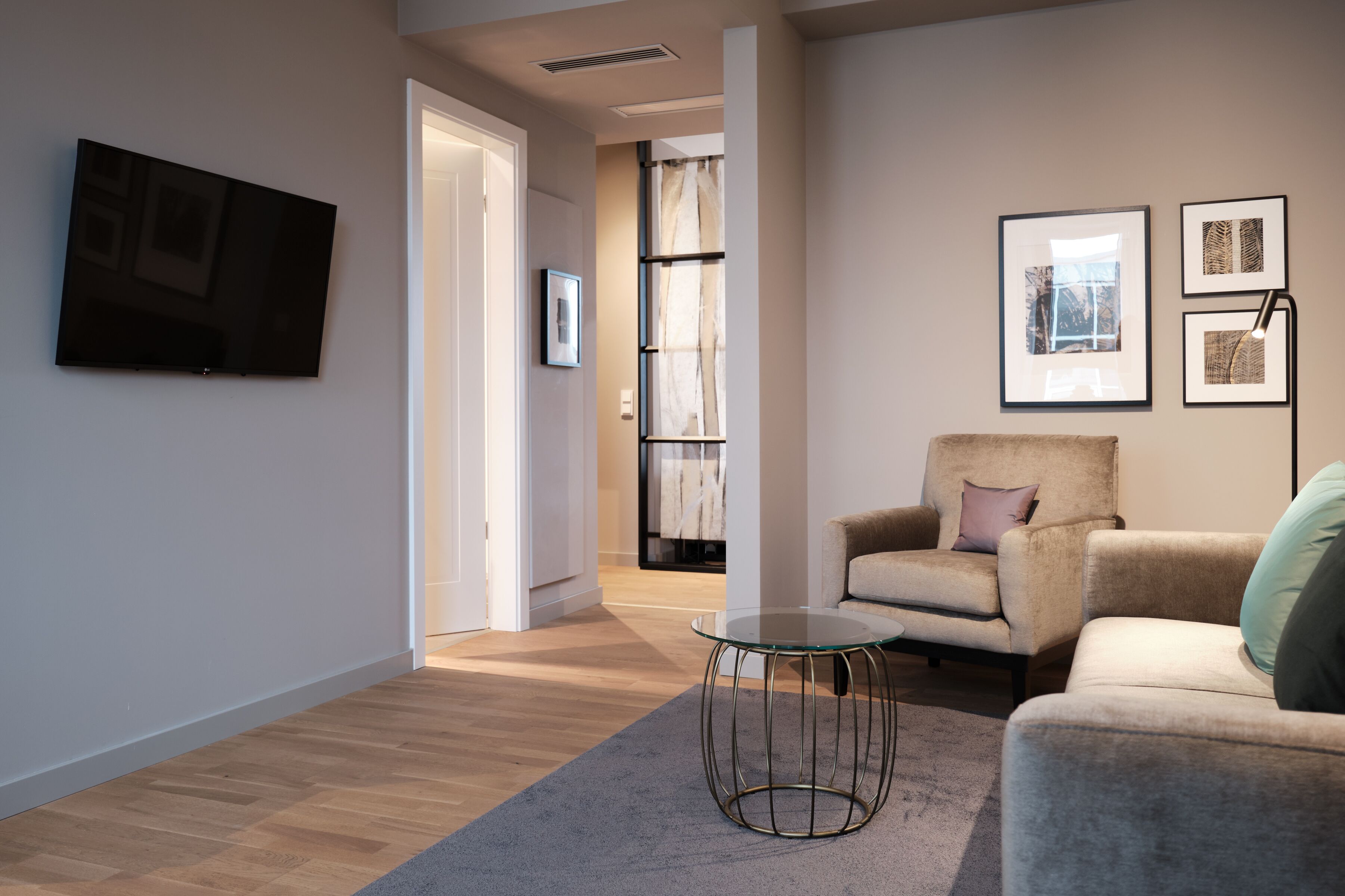 A modern living room with a flat-screen TV, a comfortable armchair, a sofa, and a small round table.