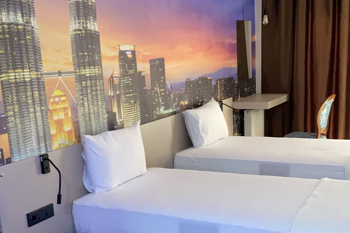 A hotel room with two beds, a wall mural of a city skyline, a ceiling fan, and a wooden chair.