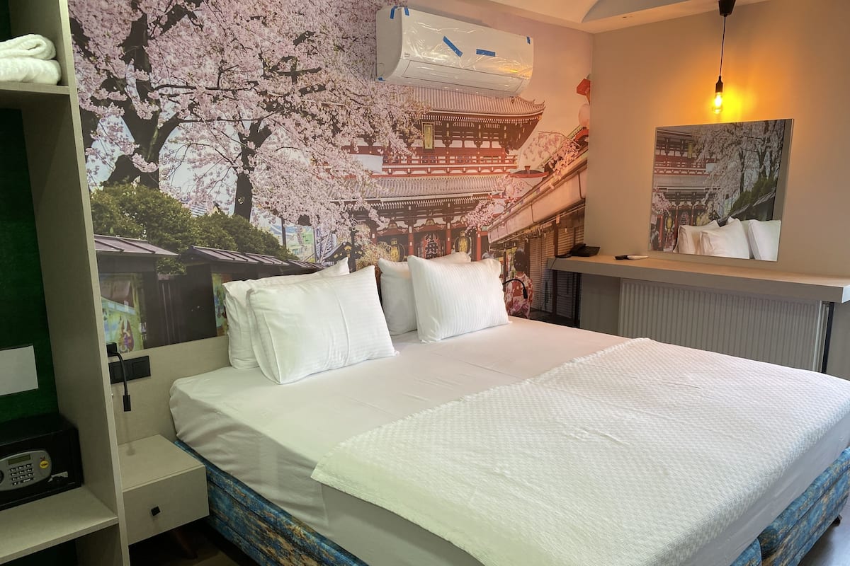 A neatly made bed with white linens in a room with a mural of cherry blossoms and a traditional building.