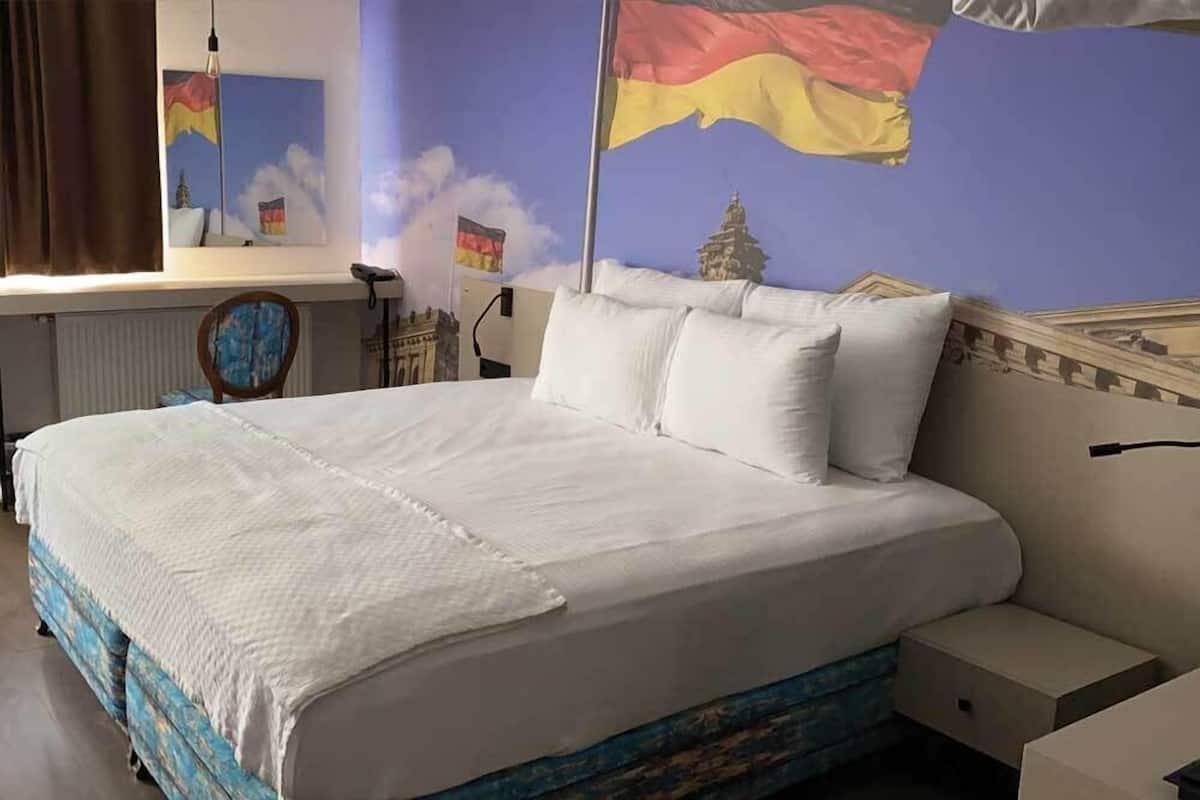 A bed with white bedding, a nightstand, and a wall with a flag and a building mural.