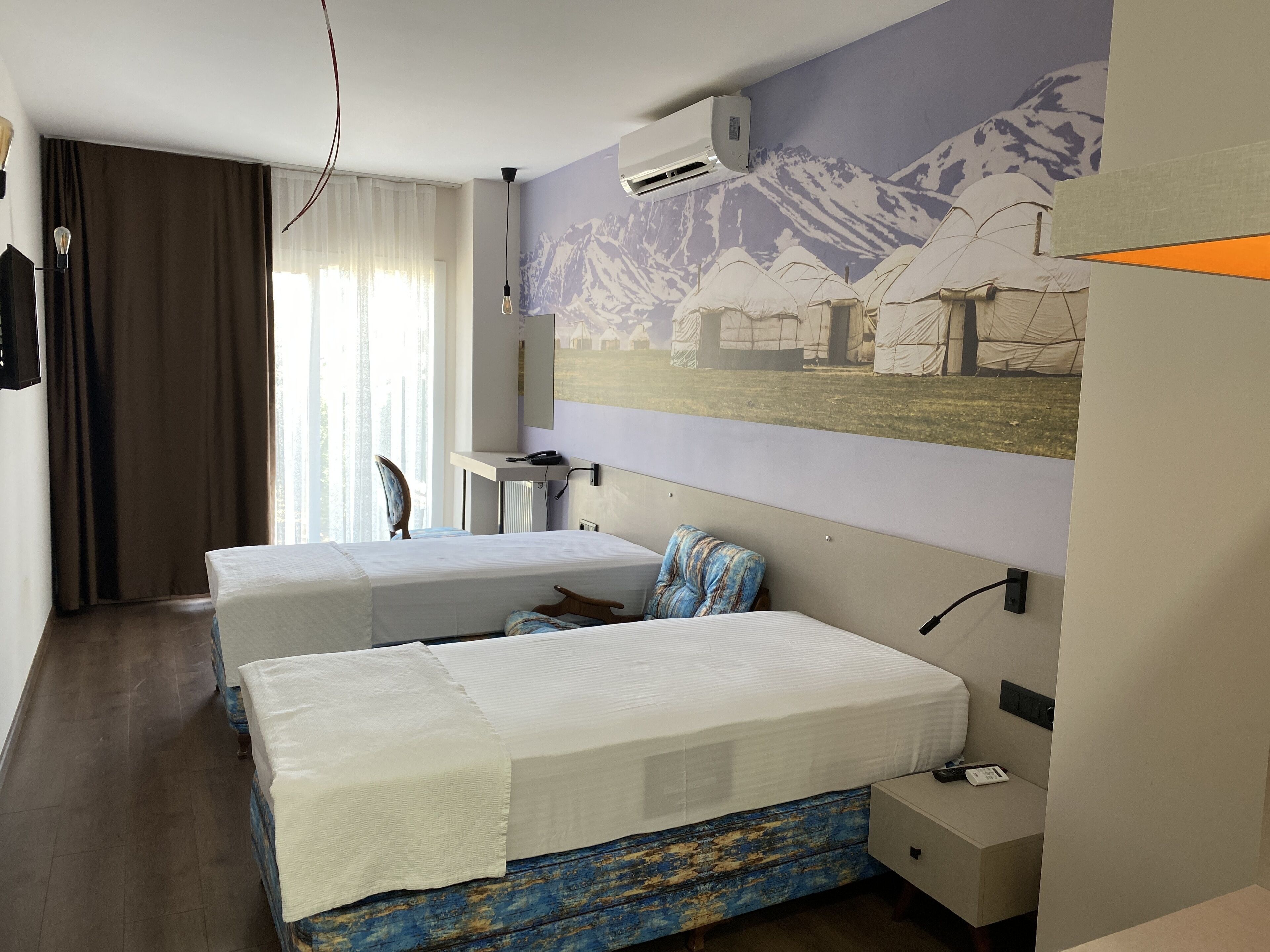 Habitación de hotel con dos camas, un escritorio, una silla, aire acondicionado instalado en la pared y televisor también en la pared.