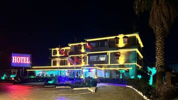 Un hotel con un llamativo letrero que dice 'HOTEL', varias banderas e iluminación exterior brillante.
