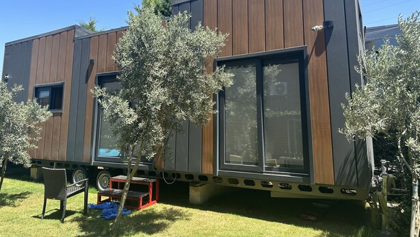 A modern mobile home with a wooden exterior, large windows, and a small patio area with a chair and table. - Ofuro World Hotel Spa (Izmir)