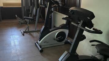 Een fitnessruimte met hometrainers, krachtapparaten en een raam met zonwering.