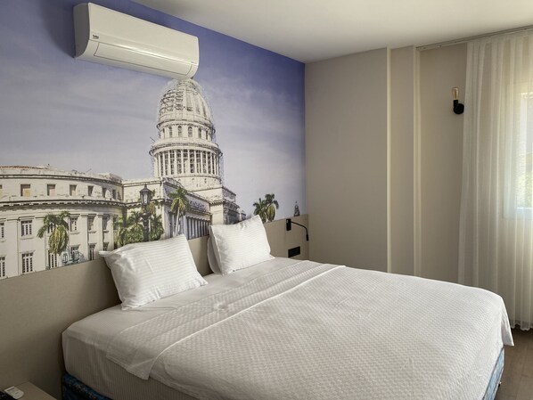 Habitación de hotel con una cama grande, aire acondicionado de pared y un mural de un edificio.