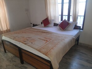Een slaapkamer met een bed, twee kussens, een nachtkastje en een raam met gordijnen.