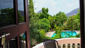 Vista desde un balcón con vistas a una piscina rodeada de exuberante vegetación y montañas.