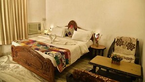 Un dormitorio con una cama de madera, una mesita de noche con un florero, una silla con un cojín floral y una ventana con cortinas.