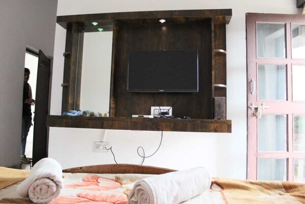 A hotel room with a bed, a TV mounted on a wooden shelf, and a door with glass panels. - Green Park Resort (Pushkar)
