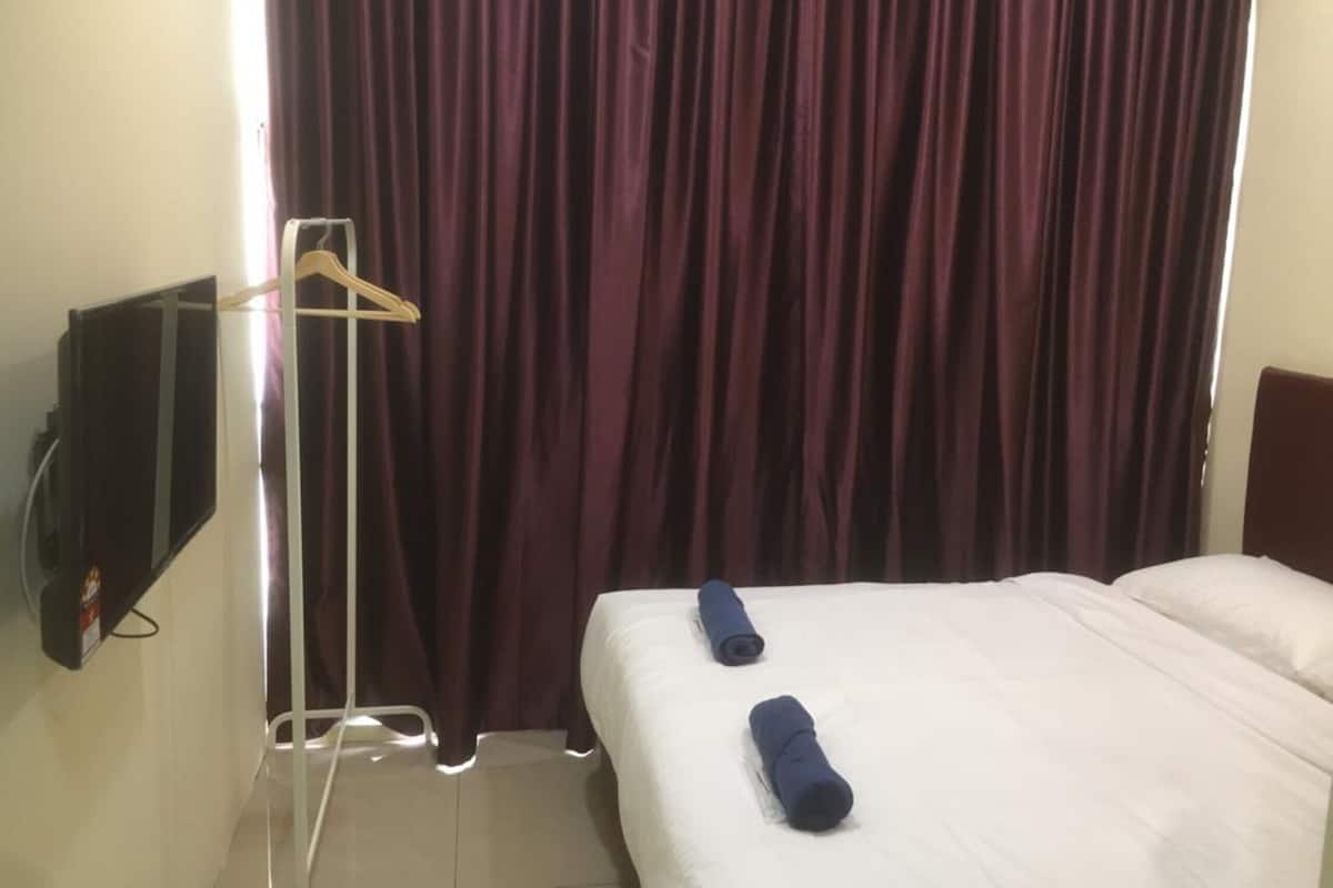 A hotel room with a bed, two rolled-up towels, a TV mounted on the wall, and a curtain.