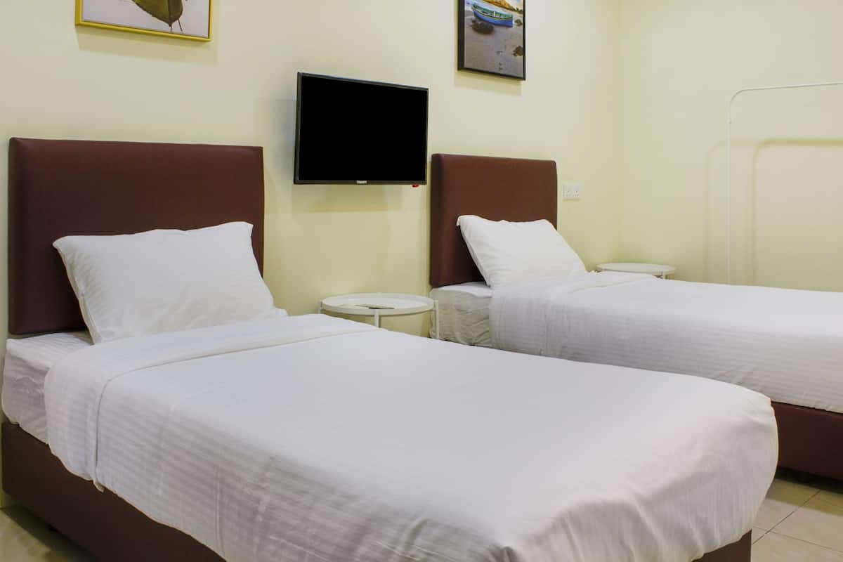 Two single beds with white linens, a flat-screen TV mounted on the wall, and a small round table between them.