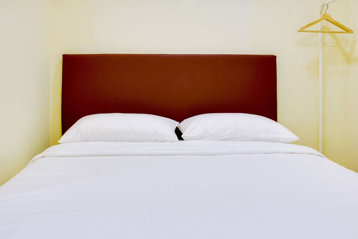 A neatly made bed with white linens and a dark headboard in a room with light yellow walls.