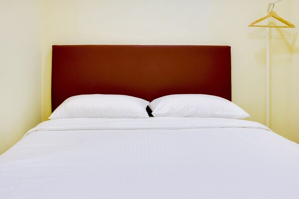 A neatly made bed with white linens and a dark headboard in a room with light yellow walls. - OYO 90090 Roselyn Inn 2 (Pasir Gudang)
