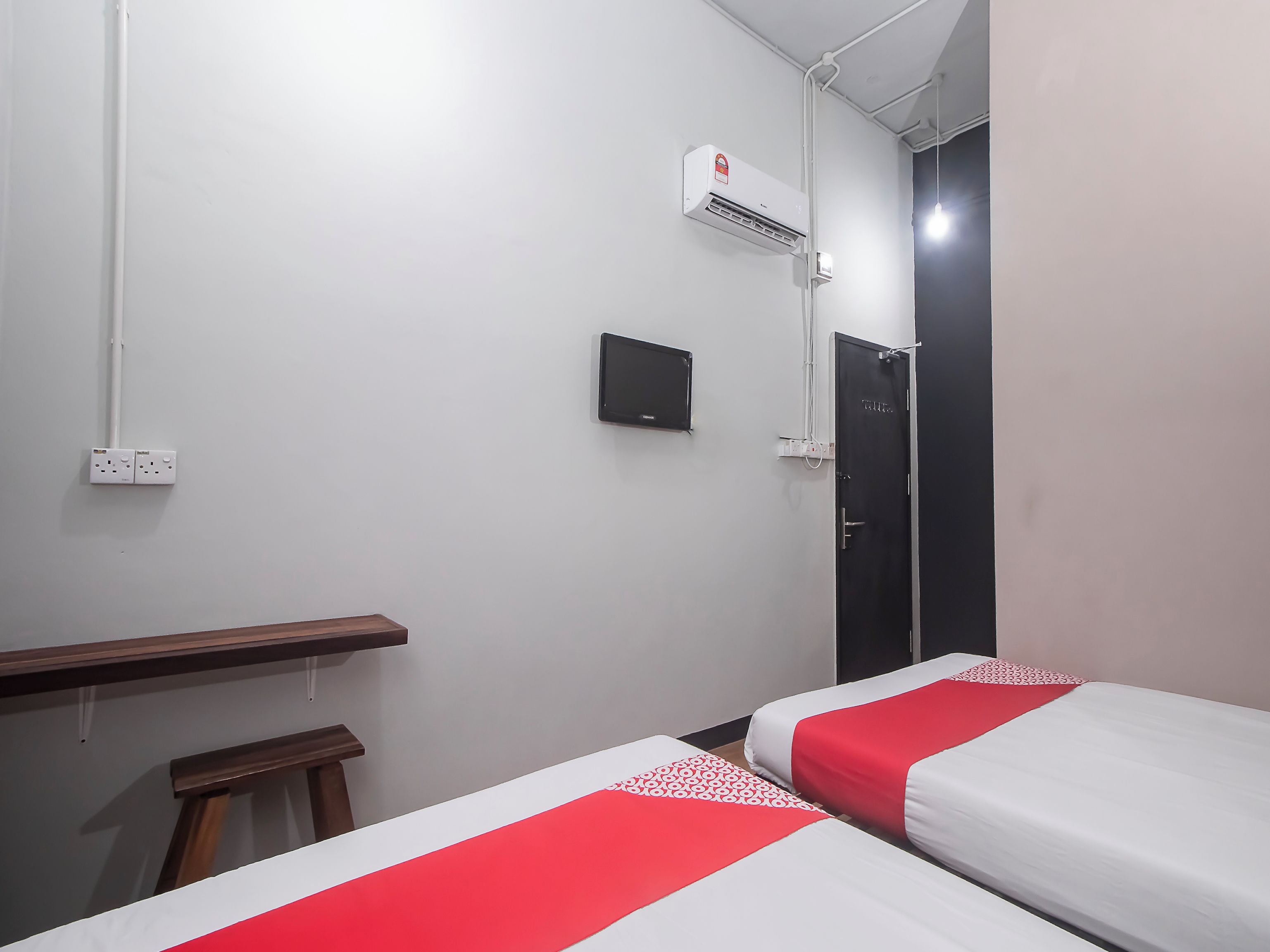 A hotel room with two beds, a desk, a chair, an air conditioning unit, a TV, and a door.