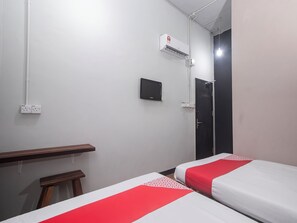 A hotel room with two beds, a desk, a chair, an air conditioning unit, a TV, and a door.