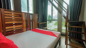 A room with a bed, a wooden headboard, a window with a view of a road, and a wooden ladder.