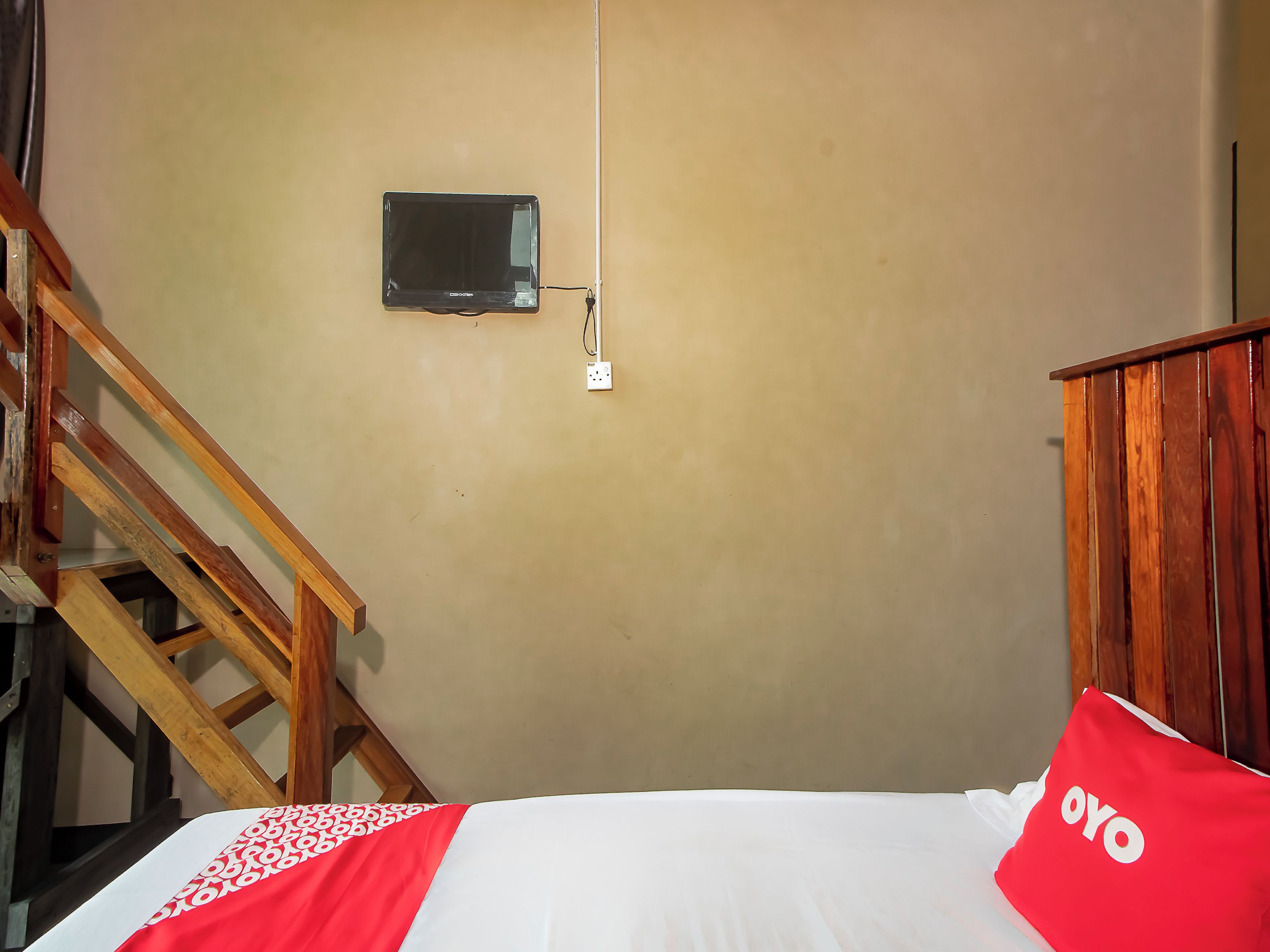 A room with a bed, a wooden staircase, a wall-mounted television, and a power outlet.