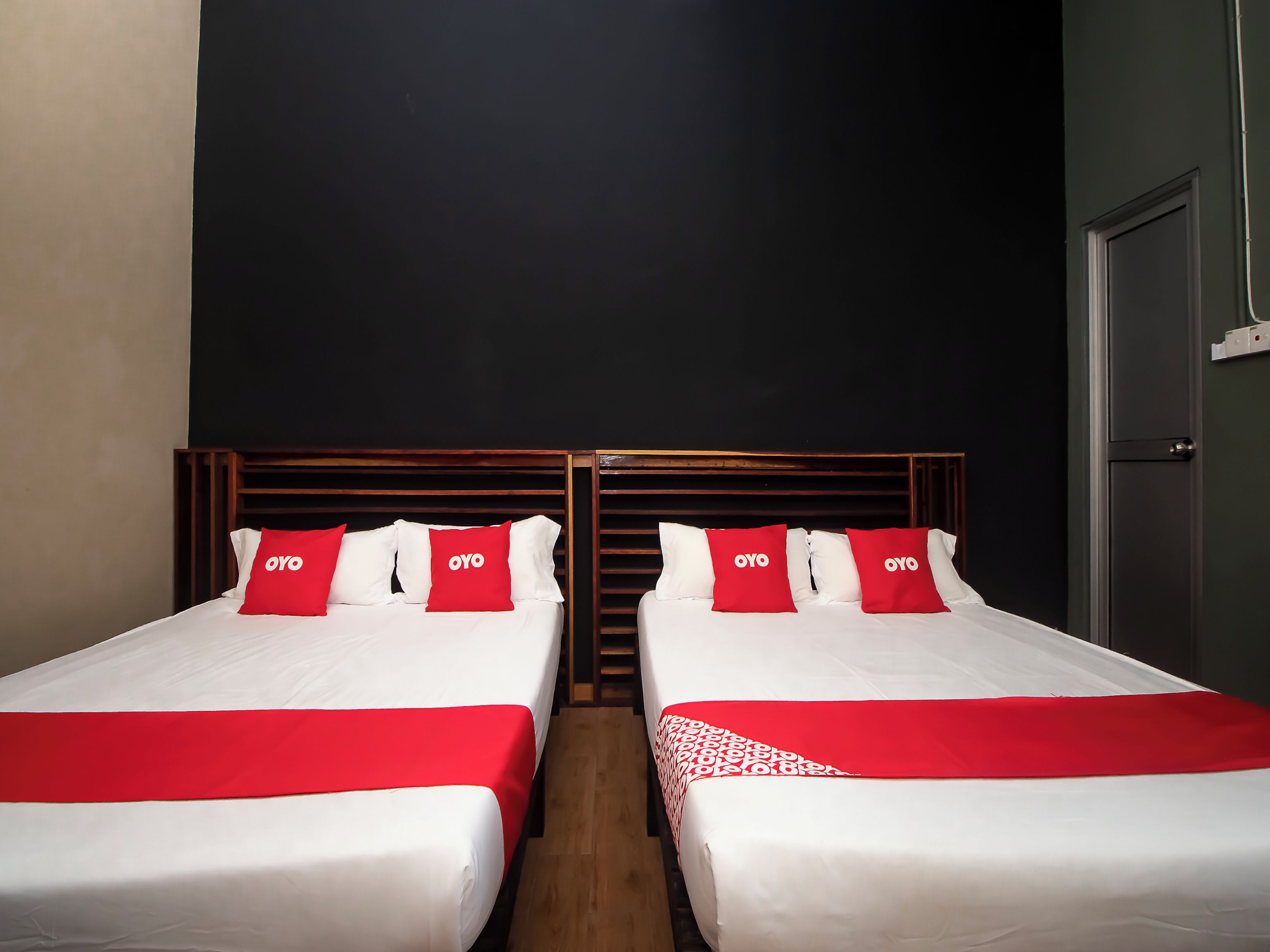 A hotel room with two beds, each with white bedding and red accents, including pillows and a red runner.