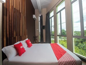 A hotel room with a large bed, a wooden wall panel, an air conditioning unit, and a view of greenery through the windows. - OYO 90094 Hi Inn 3 (Sibu)
