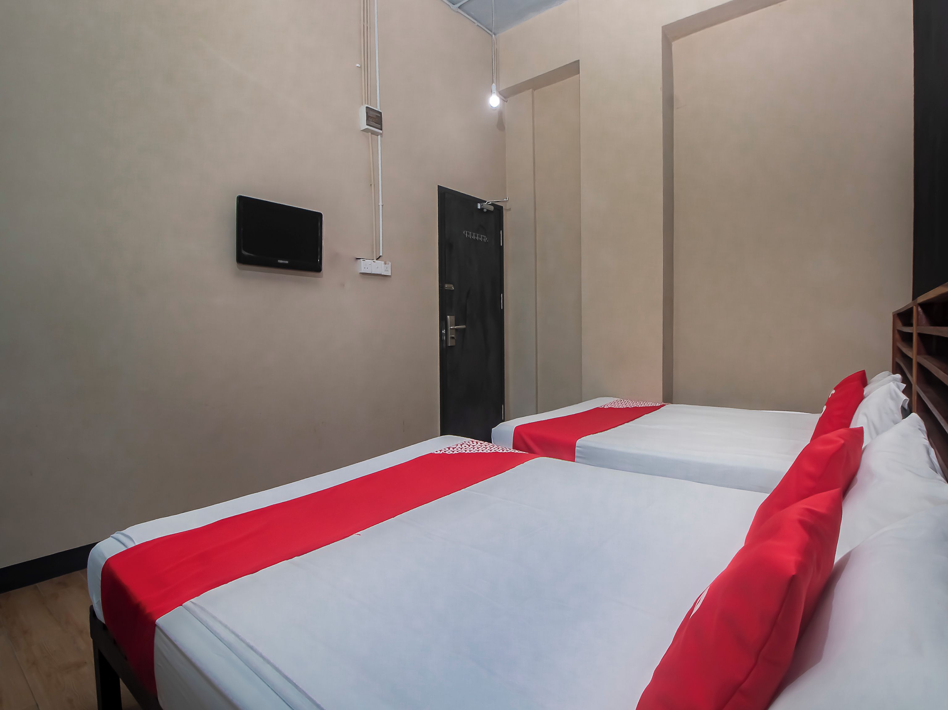 A hotel room with two beds, each with a red and white bedspread, a flat-screen TV mounted on the wall, and a door with a handle.