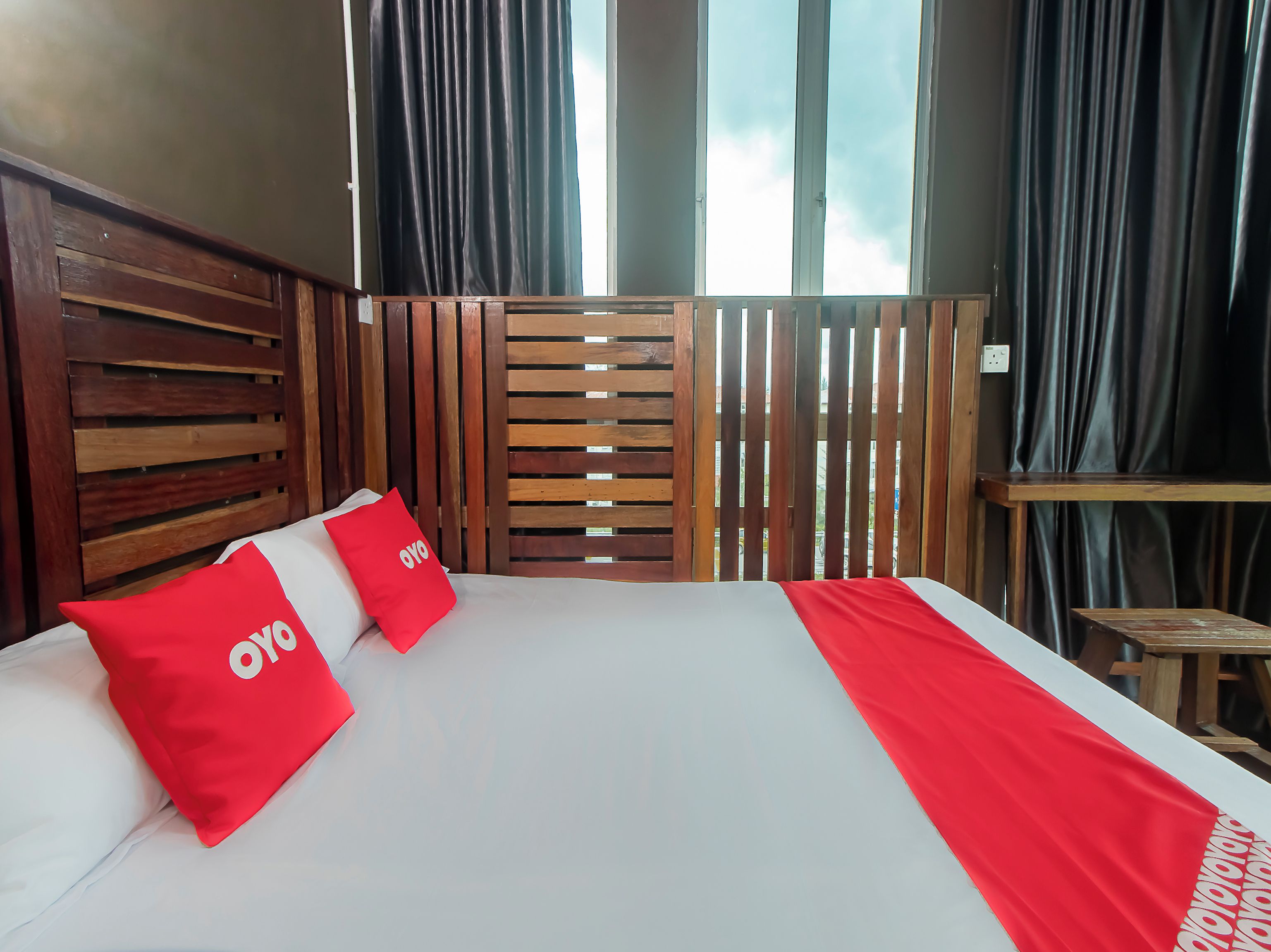 A hotel room with a wooden headboard, two red pillows with 'OYO' branding, a white bedspread, and a red throw.