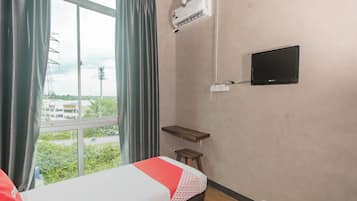 A hotel room with two beds, a TV, an air conditioning unit, and a window with curtains.