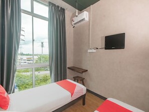 Una camera d'albergo con due letti, una televisione, un condizionatore d'aria e una finestra con tende.
