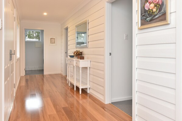 A hallway with wooden flooring, white walls, a white console table with a vase, and a mirror above it.