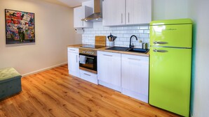 A modern kitchen with white cabinets, a green refrigerator, wooden flooring, and a painting on the wall. - Oberreute - Modern vacation apartment with panoramic views of the Allgäu (Oberreute)