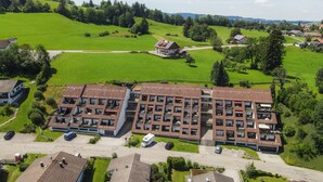 A multi-story residential building with a flat roof, surrounded by green fields and trees. - Oberreute - Modern vacation apartment with panoramic views of the Allgäu (Oberreute)